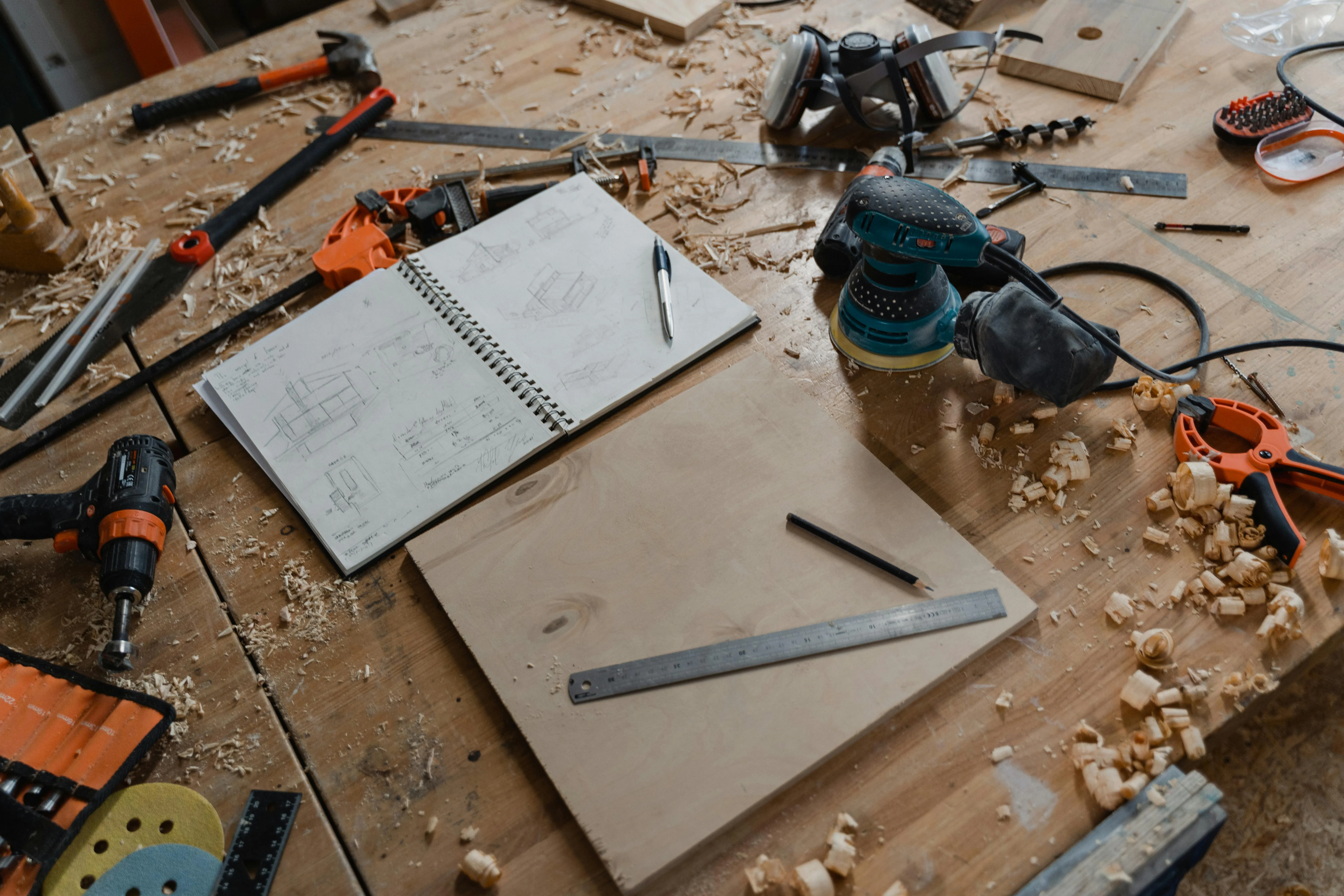 Construction tools, pens, and notebook on wooden table.